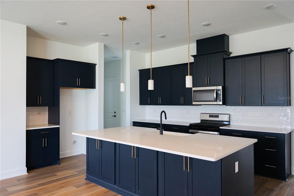 A modern kitchen features dark blue cabinets, a white quartz island, and gold pendant lights — 2 TREE HOUSE DRIVE, PALM COAST, FL
