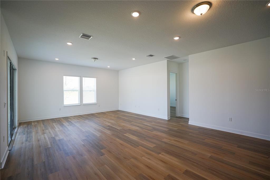 A spacious, empty room features white walls, recessed lighting, and wood-look flooring — 2 TREE HOUSE DRIVE, PALM COAST, FL