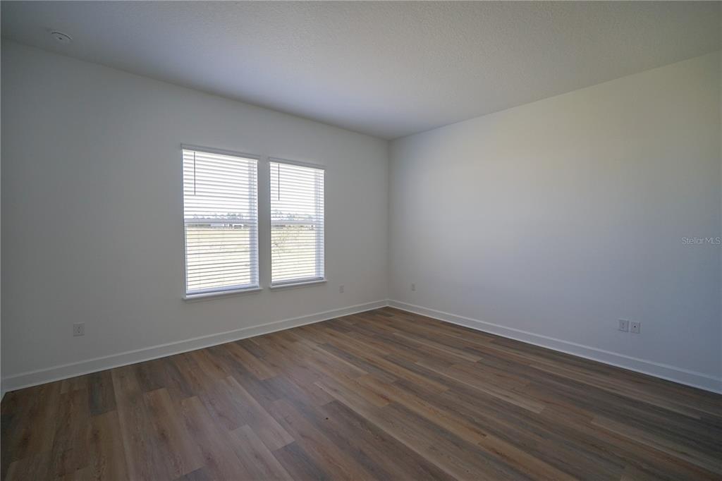 An empty bedroom features white walls, wood-look flooring, and two windows with blinds — 2 TREE HOUSE DRIVE, PALM COAST, FL