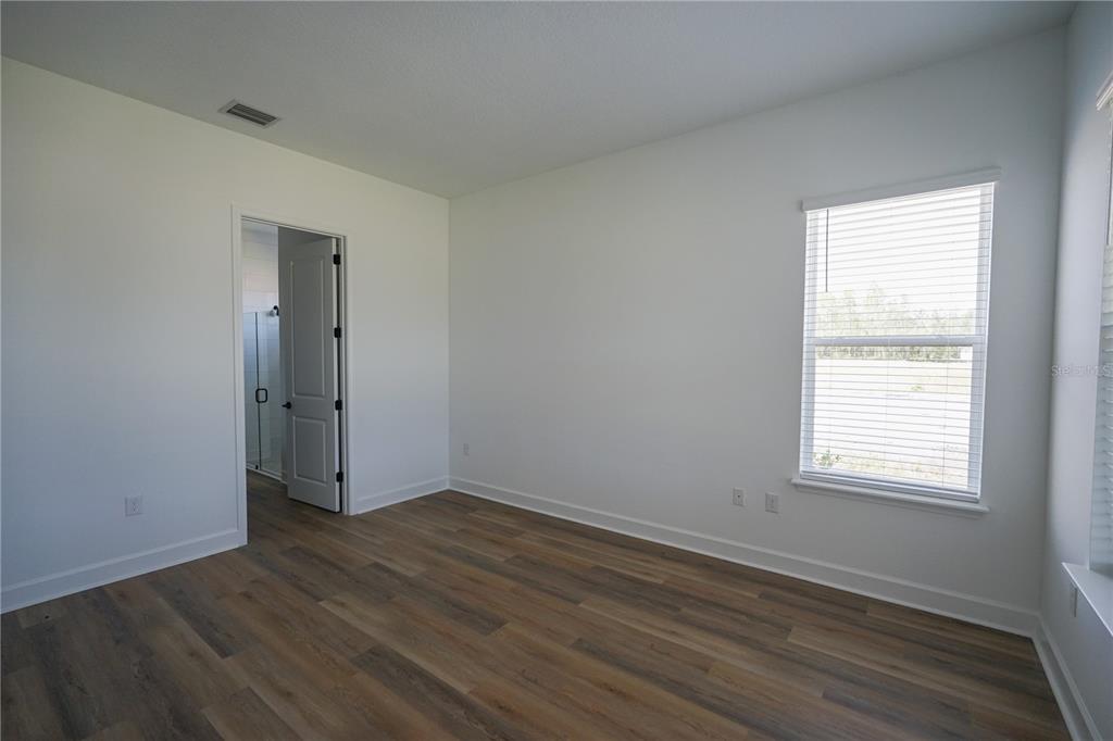An empty bedroom features white walls, wood-look flooring, a window with blinds, and an open doorway — 2 TREE HOUSE DRIVE, PALM COAST, FL