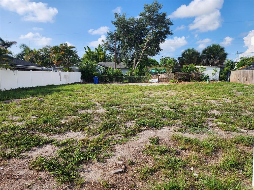 A vacant, grassy residential lot enclosed by white and wooden fences under a blue sky — 1748 31ST AVENUE N, ST PETERSBURG, FL