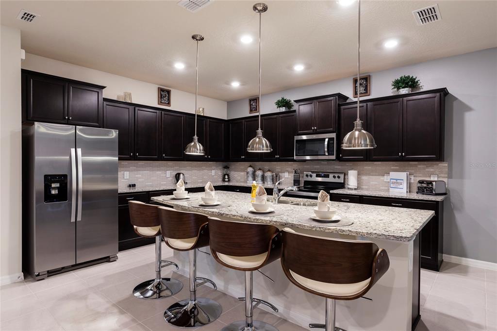 A kitchen features dark wood cabinets, granite countertops, a central island, and stainless steel appliances — 2316 LELANI CIRCLE, DAVENPORT, FL