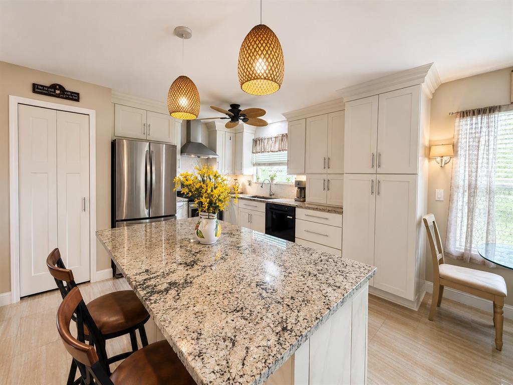 A kitchen features a granite-topped island, white cabinetry, stainless steel appliances, and two pendant lights — 1409 CALIFORNIA DRIVE, MELBOURNE, FL