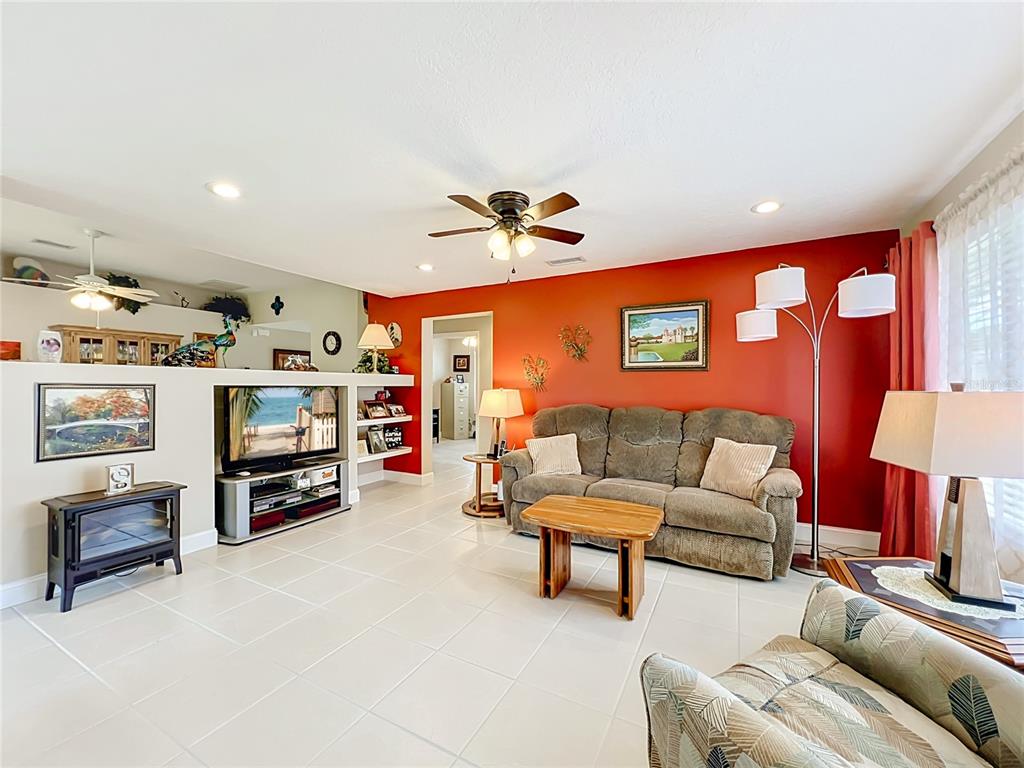 A living room features a red accent wall, a brown sofa, and white tile flooring — 1409 CALIFORNIA DRIVE, MELBOURNE, FL