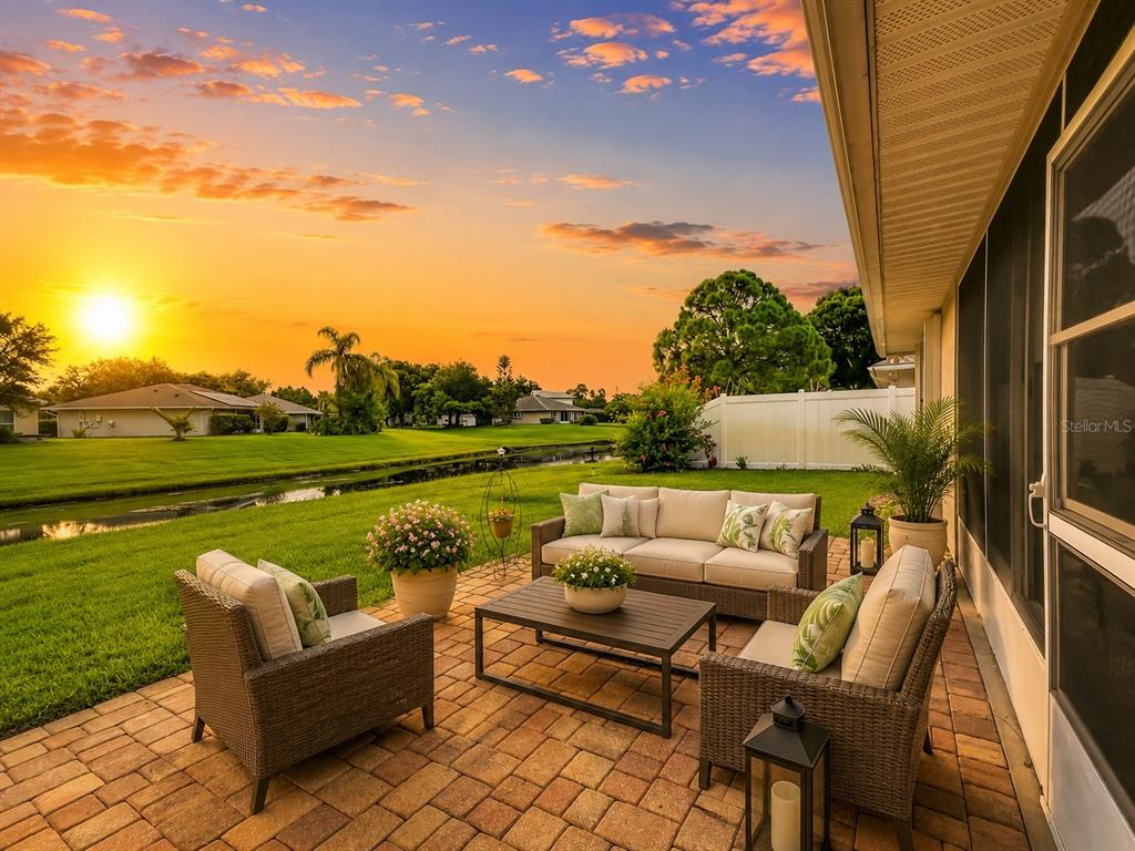 A patio with wicker furniture overlooks a grassy lawn, a canal, and a sunset sky — 1409 CALIFORNIA DRIVE, MELBOURNE, FL