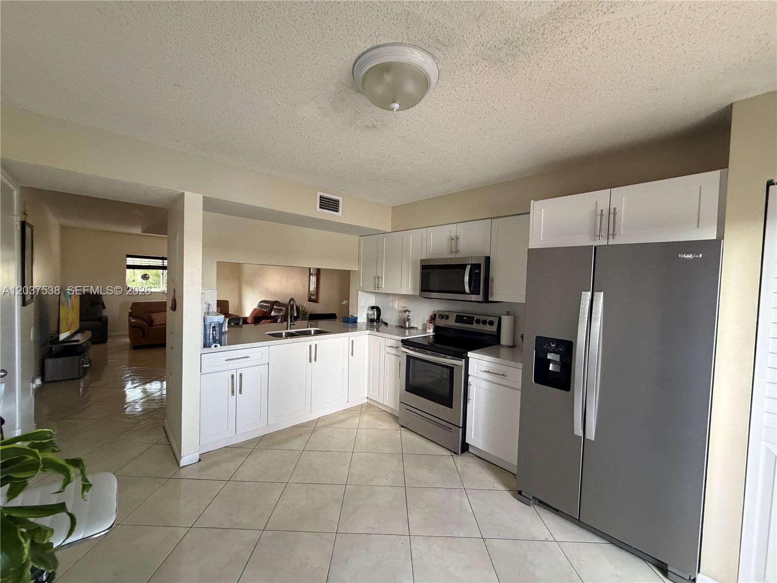 A kitchen features white cabinets, stainless steel appliances, and light-colored tile flooring — 14902 SW 82nd Ln # 205, Miami FL 33193, MIAMI, FL