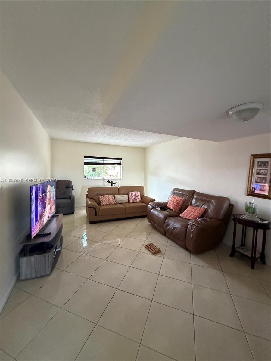A living room features light tile flooring, two brown sofas, and a television on a stand — 14902 SW 82nd Ln # 205, Miami FL 33193, MIAMI, FL