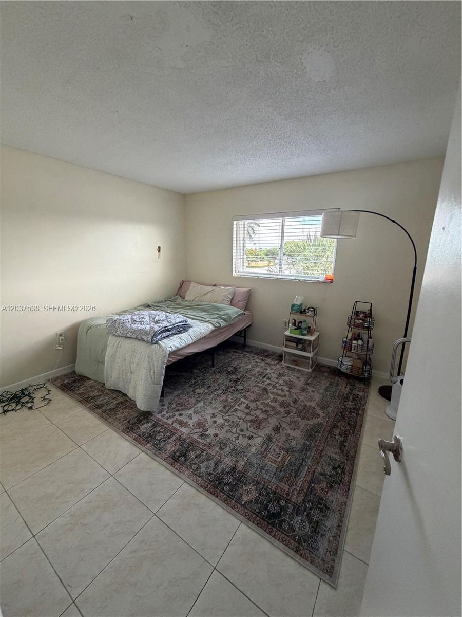A bedroom features tile flooring, a large area rug, a bed, and a floor lamp — 14902 SW 82nd Ln # 205, Miami FL 33193, MIAMI, FL