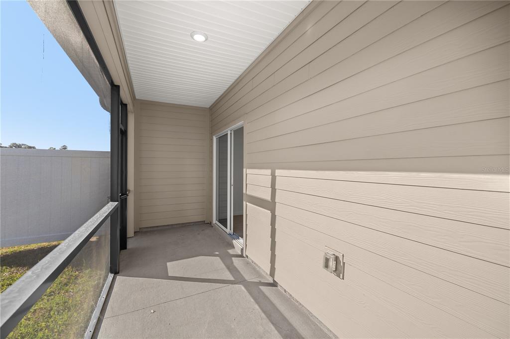 A covered, screened-in concrete patio with beige horizontal siding and a sliding glass door — 3339 SE 37TH AVENUE ROAD, OCALA, FL