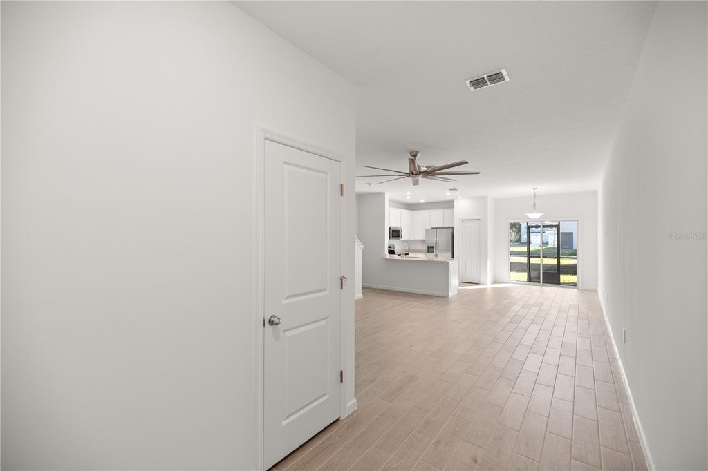 An open-concept living area features light-colored tile flooring, a white door, and a distant kitchen — 3339 SE 37TH AVENUE ROAD, OCALA, FL