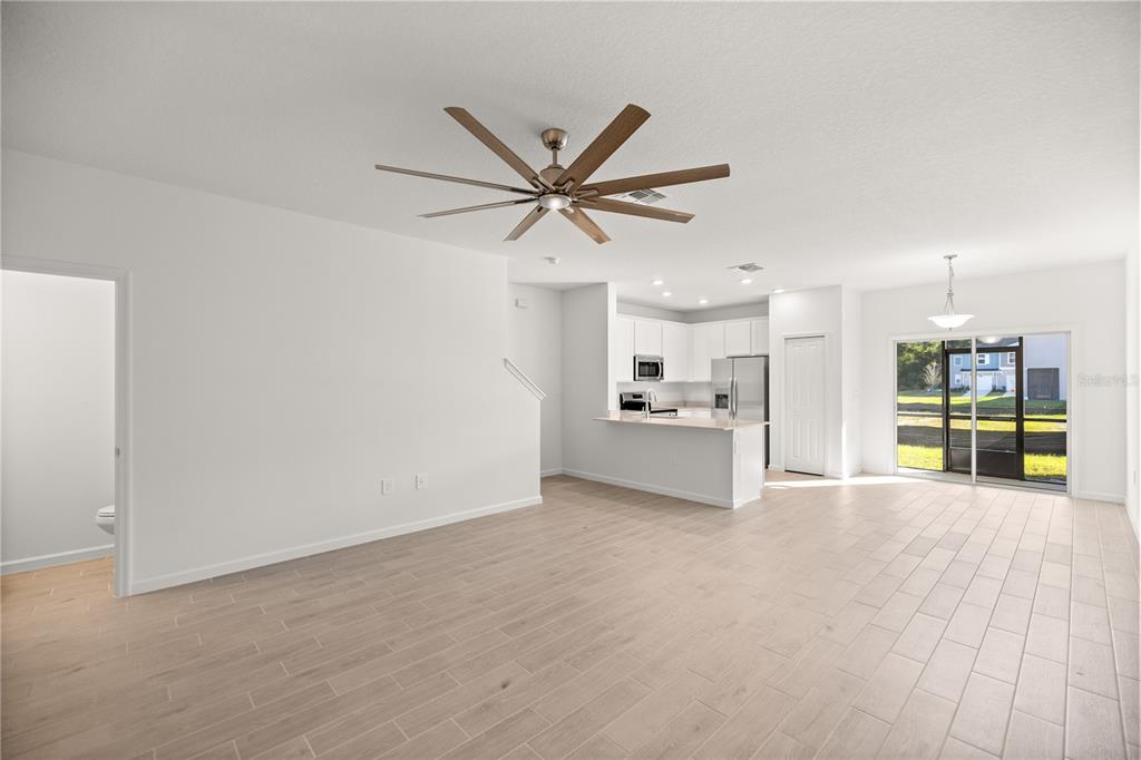 An open-concept living area features light wood-look tile floors, a ceiling fan, and a kitchen — 3339 SE 37TH AVENUE ROAD, OCALA, FL