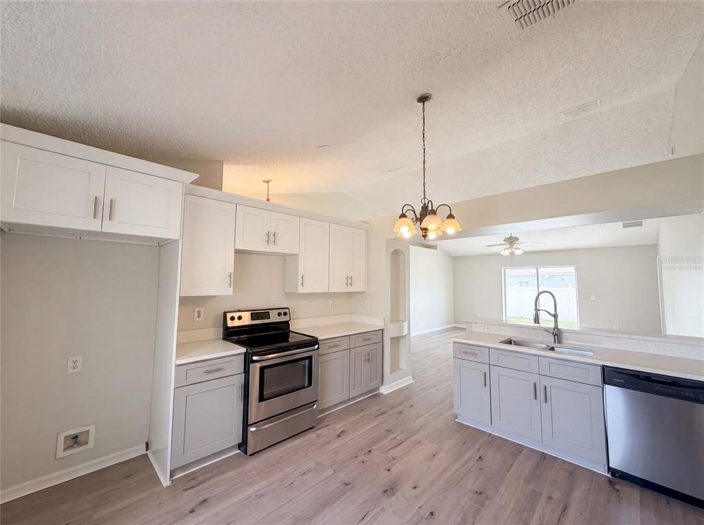 A kitchen with white upper cabinets, gray lower cabinets, stainless steel appliances, and wood-look flooring — 714 DROMEDARY DRIVE, KISSIMMEE, FL