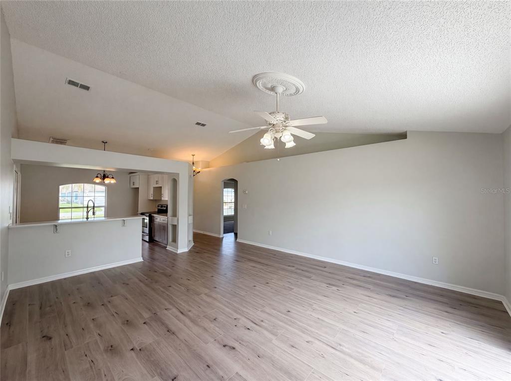 An open-concept living area features vaulted ceilings, a ceiling fan, and light wood-look flooring — 714 DROMEDARY DRIVE, KISSIMMEE, FL