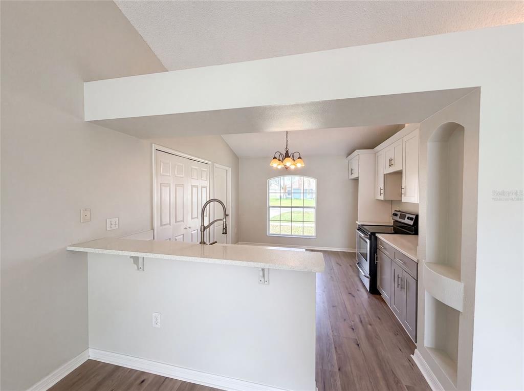 A kitchen with a breakfast bar, gray lower cabinets, white upper cabinets, and wood-look flooring — 714 DROMEDARY DRIVE, KISSIMMEE, FL
