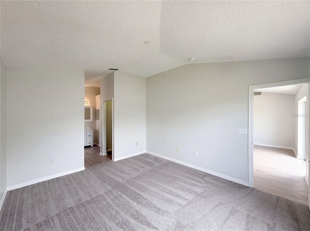 An empty bedroom with gray carpet, light-colored walls, and doorways leading to a bathroom and hallway — 714 DROMEDARY DRIVE, KISSIMMEE, FL