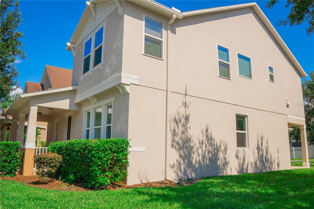 A side view of a two-story beige house with a covered porch and green landscaping — 14816 PORTER RD, WINTER GARDEN, FL