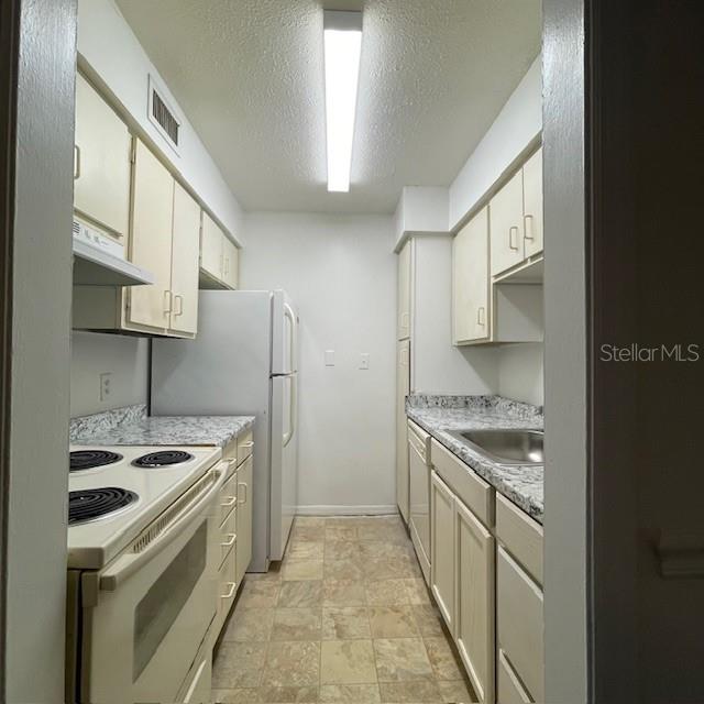 A galley kitchen features off-white cabinets, speckled laminate countertops, and a white electric range — 415 WYMORE ROAD UNIT 101, ALTAMONTE SPRINGS, FL