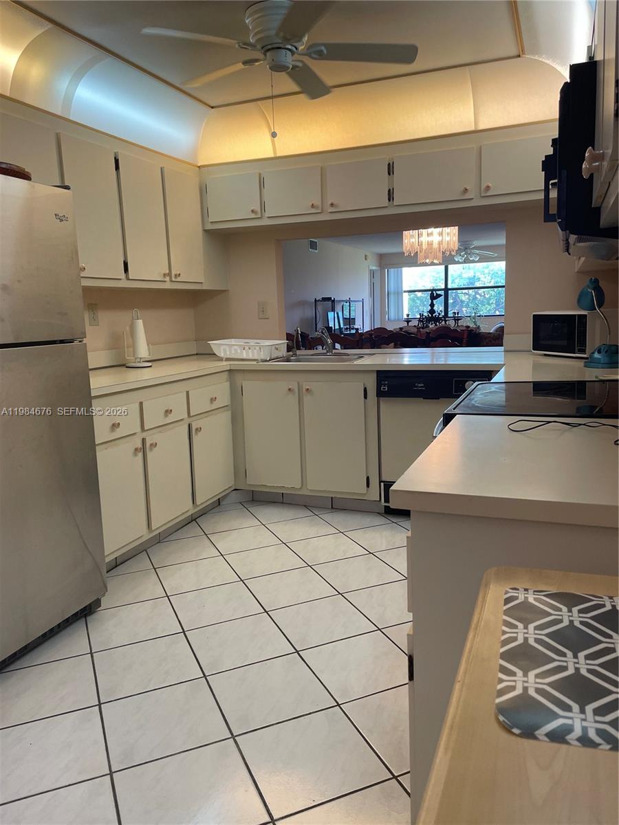 A kitchen features white cabinets, tile flooring, a stainless steel refrigerator, and a pass-through window — 2606 NW 104th Ave # 301, Sunrise FL 33322, SUNRISE, FL