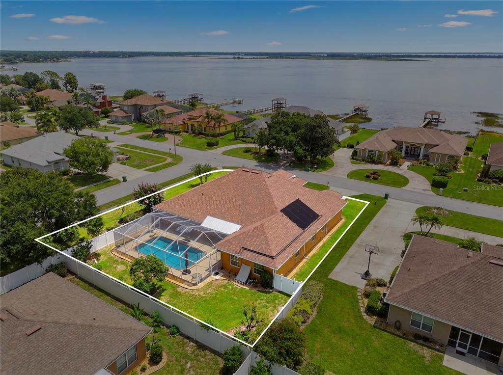 An aerial view shows a house with a pool enclosure, solar panels, and a fenced yard — 328 HAMILTON SHORES DRIVE NE, WINTER HAVEN, FL