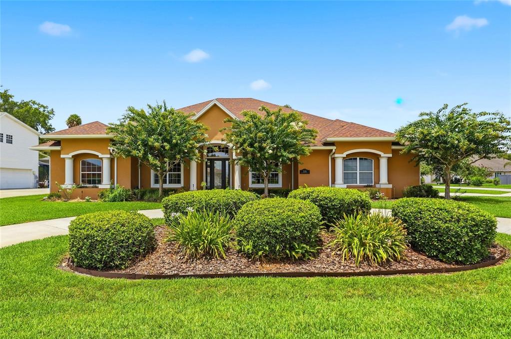 A single-story house with a tan stucco exterior, a brown roof, and landscaped front yard — 328 HAMILTON SHORES DRIVE NE, WINTER HAVEN, FL