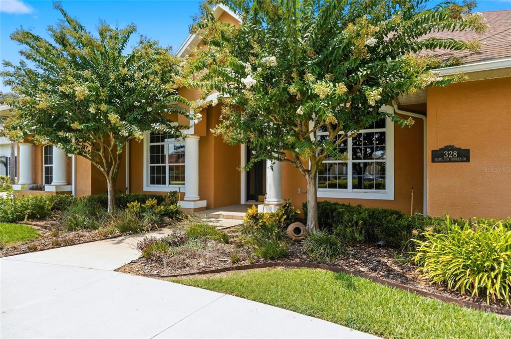 The exterior of a single-story house features a tan stucco facade, white columns, and landscaping — 328 HAMILTON SHORES DRIVE NE, WINTER HAVEN, FL