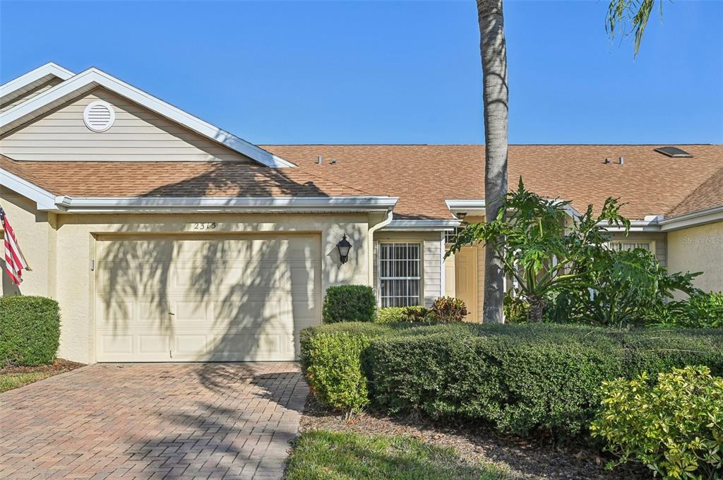 A single-story house with a beige stucco exterior, a brick driveway, and a garage — 2315 NEW ORCHARD COURT, SUN CITY CENTER, FL