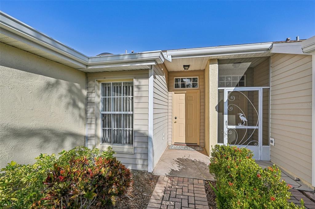 The exterior of a house features a tan front door, a screened entryway, and landscaping — 2315 NEW ORCHARD COURT, SUN CITY CENTER, FL