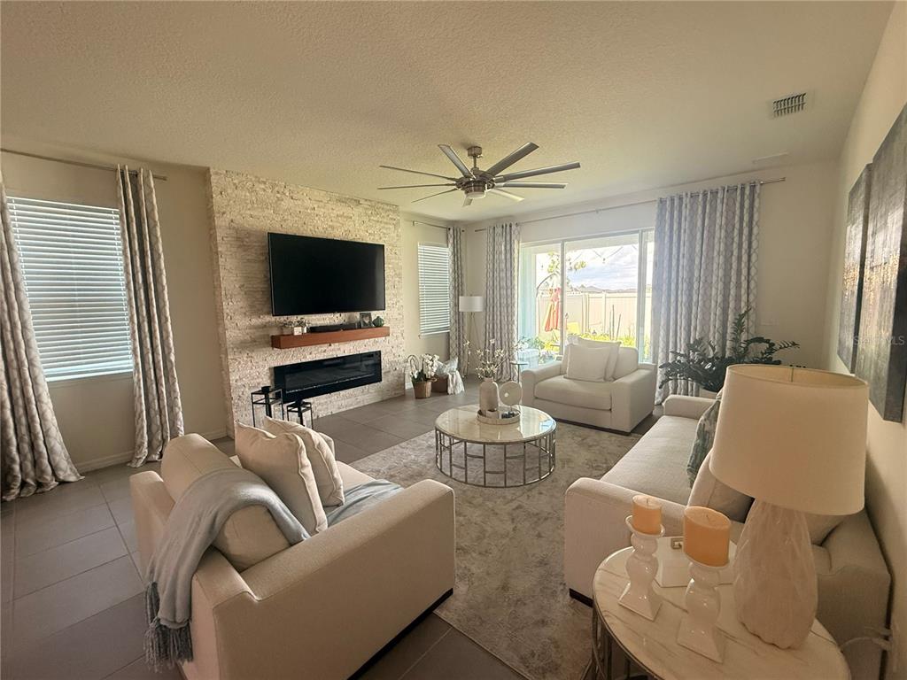 A living room features a stone fireplace wall, neutral furniture, and large windows with curtains — 988 VINEYARD RIDGE ROAD, MINNEOLA, FL
