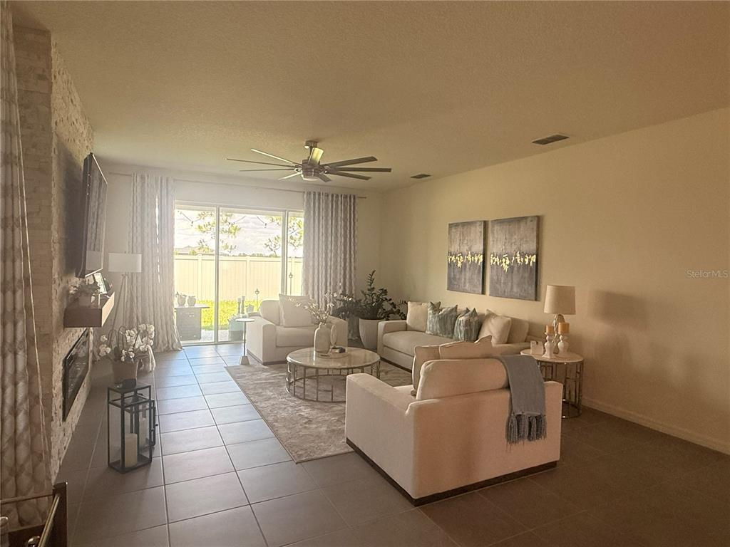 A living room features tile flooring, a stone fireplace, neutral furniture, and sliding glass doors — 988 VINEYARD RIDGE ROAD, MINNEOLA, FL