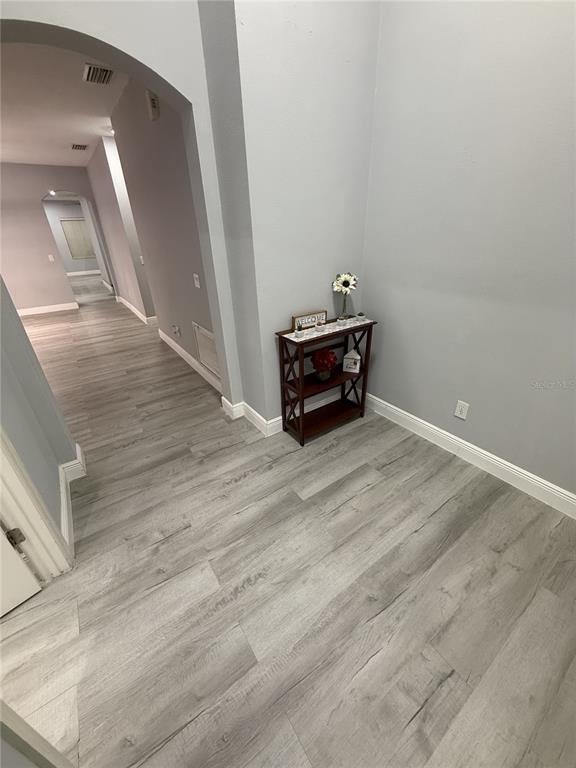 A hallway with light gray wood-look flooring leads to an arched entryway with a small shelf — 16321 SAINT AUGUSTINE STREET, CLERMONT, FL