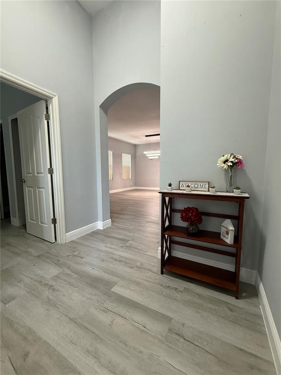 A hallway with light wood-look flooring leads through an arched doorway into an open room — 16321 SAINT AUGUSTINE STREET, CLERMONT, FL
