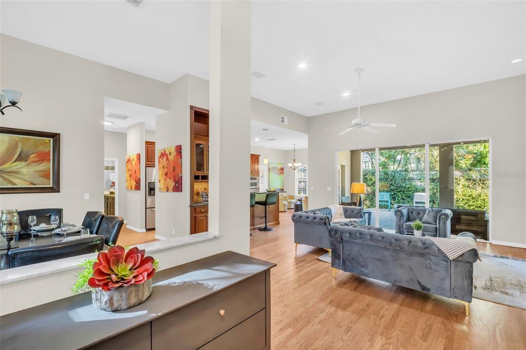 An open-concept living and dining area features hardwood floors, gray tufted sofas, and a kitchen — 2270 BARBARA DRIVE, CLEARWATER, FL