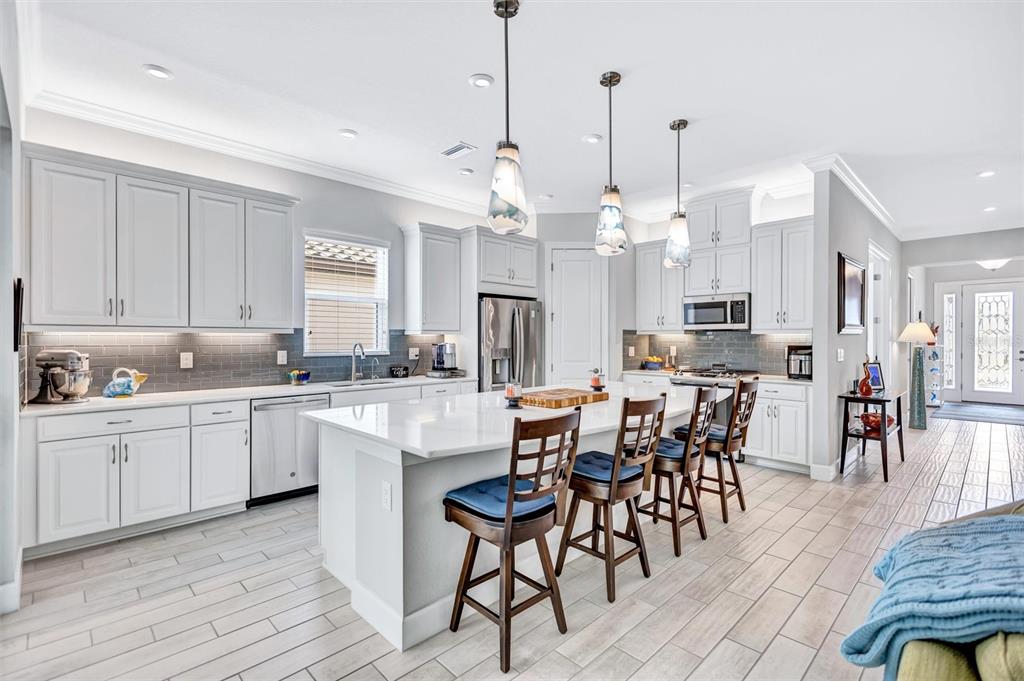 A modern kitchen features white cabinetry, a large center island with bar stools, and tile flooring — 5880 SEMOLINO STREET, NOKOMIS, FL