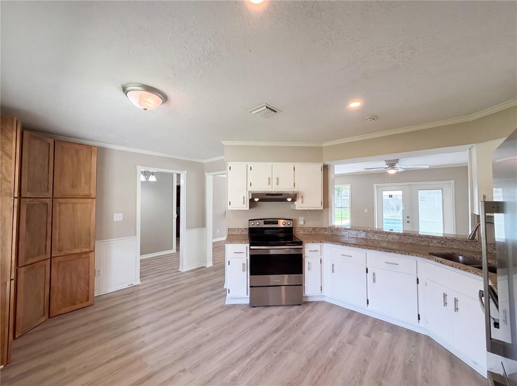 A kitchen features white cabinets, stainless steel appliances, granite countertops, and light wood-look flooring — 1770 NE 37TH STREET, OCALA, FL