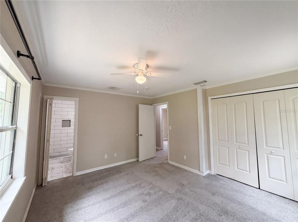 A bedroom with gray carpet, beige walls, a ceiling fan, and an attached bathroom — 1770 NE 37TH STREET, OCALA, FL