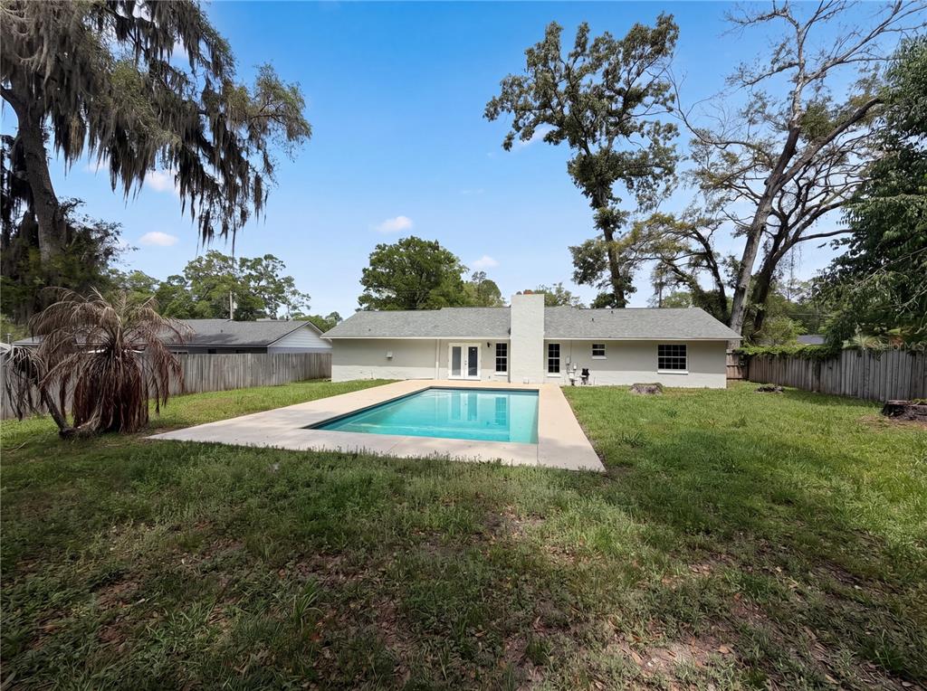 A backyard view of a single-story house featuring a rectangular swimming pool and lawn — 1770 NE 37TH STREET, OCALA, FL