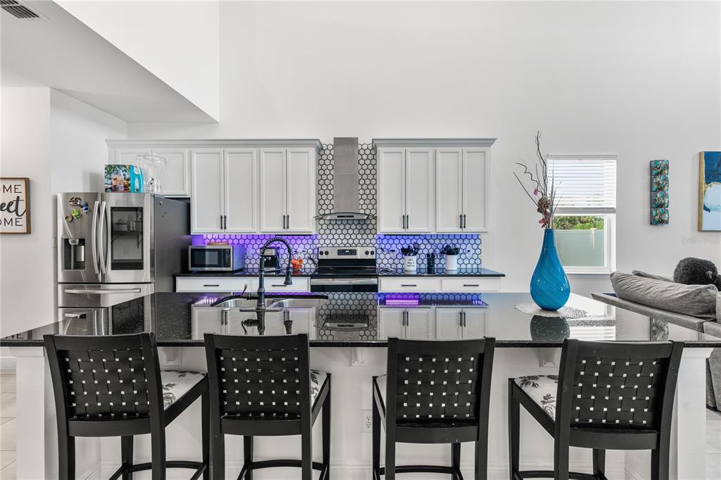 A modern kitchen features white cabinets, black countertops, a hexagonal tile backsplash, and four barstools — 5637 BEGGS ROAD, ST CLOUD, FL