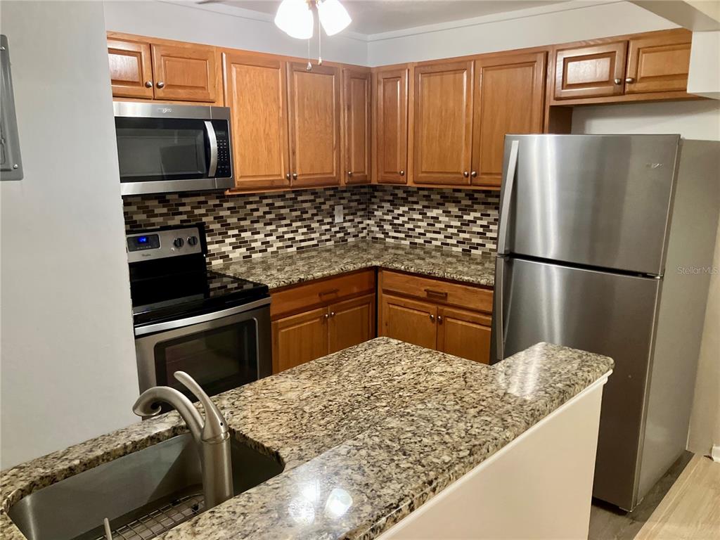 A kitchen features wood cabinets, granite countertops, stainless steel appliances, and a tiled backsplash — 100 SWEETGUM WOODS COURT UNIT 4A, DELTONA, FL