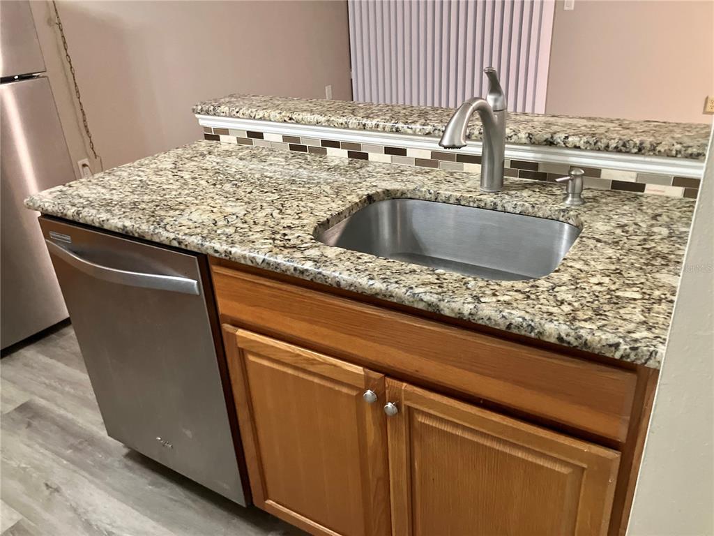 A kitchen island features a stainless steel sink, faucet, and dishwasher with granite countertops — 100 SWEETGUM WOODS COURT UNIT 4A, DELTONA, FL