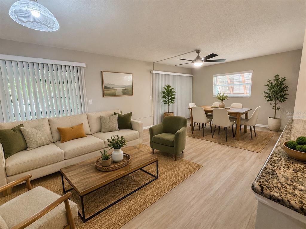 This living and dining room features light wood-look flooring, a neutral sofa, and a dining set — 100 SWEETGUM WOODS COURT UNIT 4A, DELTONA, FL