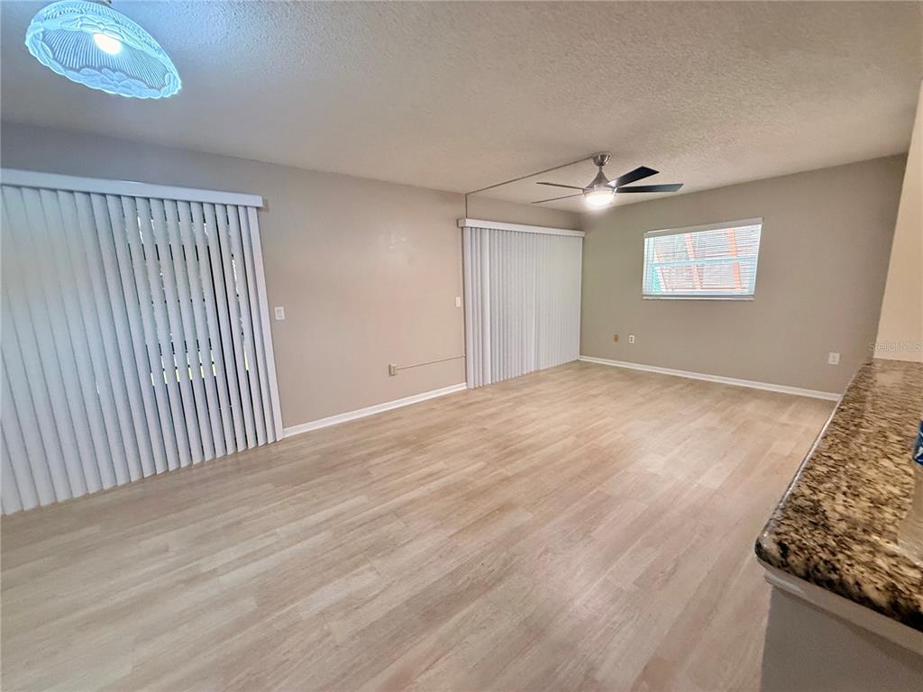 An empty living room features light wood-look flooring, vertical blinds, and a ceiling fan — 100 SWEETGUM WOODS COURT UNIT 4A, DELTONA, FL