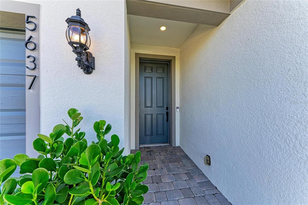 A front entryway features a dark gray door, a wall-mounted lantern, and a paver walkway — 5637 SILVERSIDE PINE COURT, BRADENTON, FL