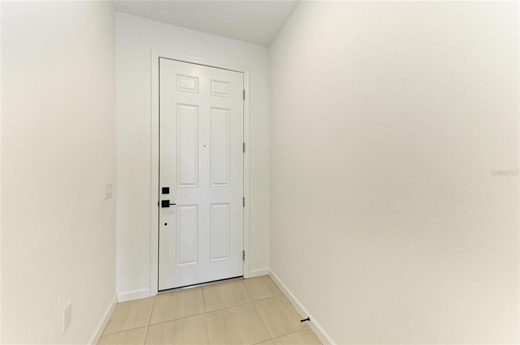 A white front door with black hardware sits in a small entryway with tiled floors — 5637 SILVERSIDE PINE COURT, BRADENTON, FL