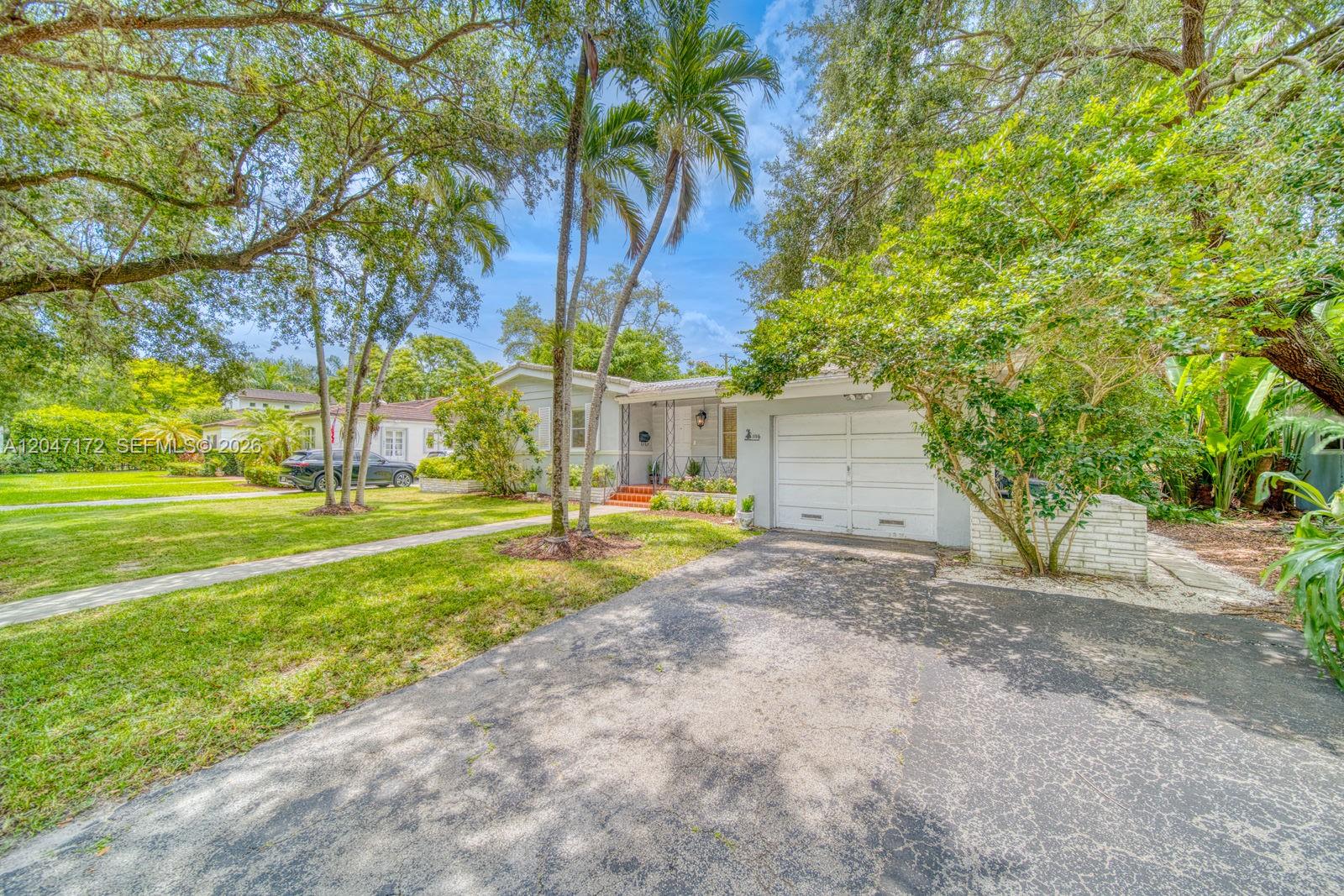 A single-story house with a white garage, a paved driveway, and mature trees in front — 1116 Almeria Ave, Coral Gables FL 33134, CORAL GABLES, FL