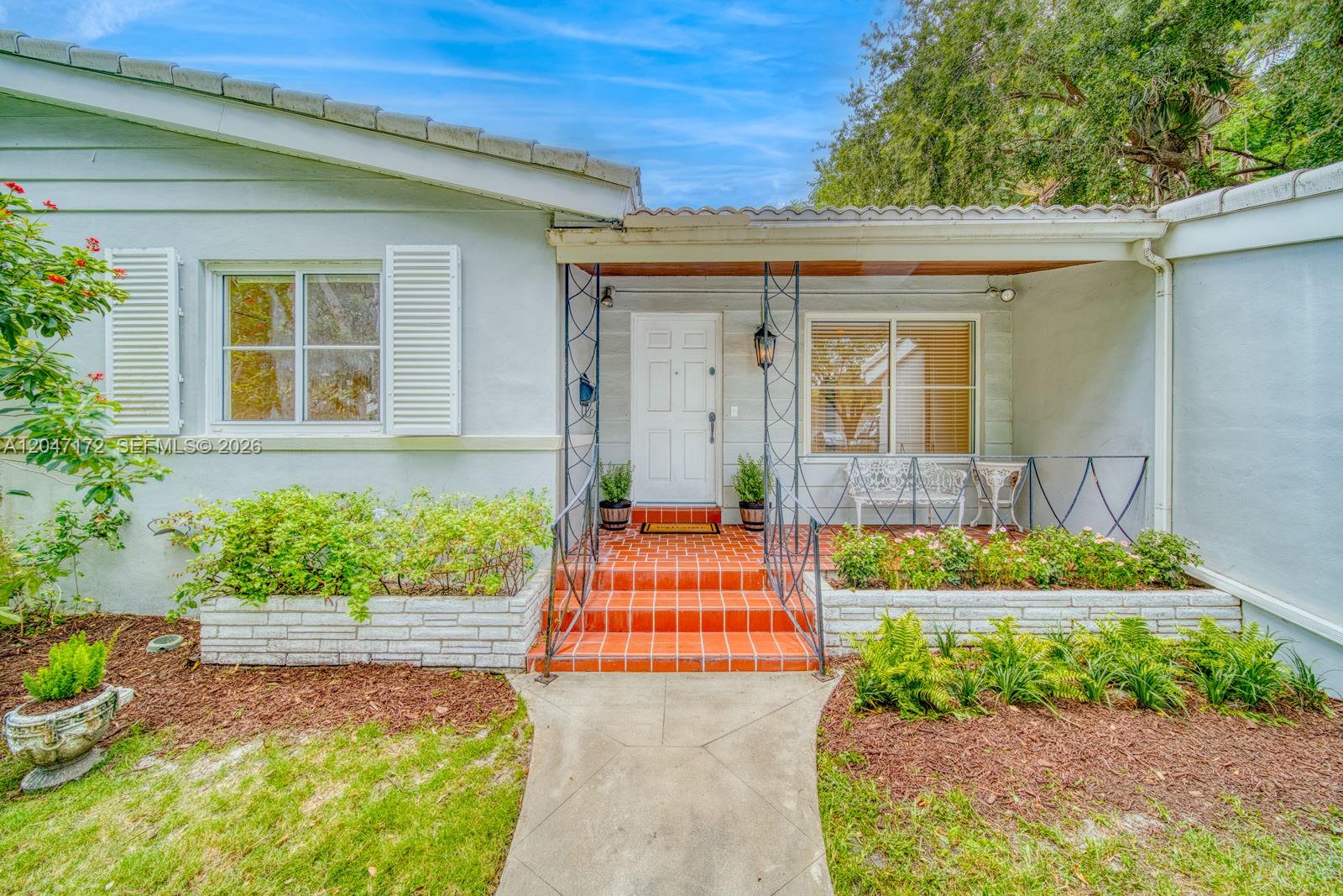 The exterior of a light-colored house features a red-tiled porch, metal railings, and landscaping — 1116 Almeria Ave, Coral Gables FL 33134, CORAL GABLES, FL