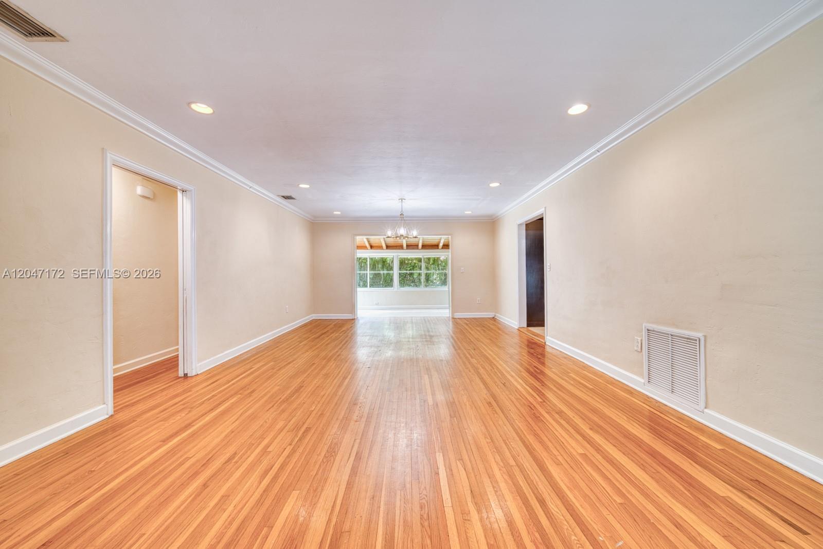 An empty living room features hardwood floors, recessed lighting, and a doorway to a sunroom — 1116 Almeria Ave, Coral Gables FL 33134, CORAL GABLES, FL