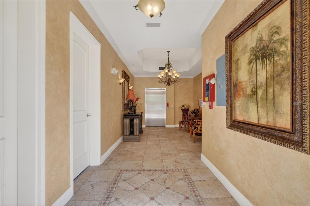 A hallway features tan textured walls, tile flooring, a chandelier, and a stainless steel elevator — 40 CASA BELLA CIRCLE UNIT 1102, PALM COAST, FL