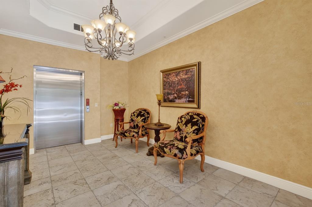 A lobby area features a metal elevator, two patterned chairs, a small table, and chandelier — 40 CASA BELLA CIRCLE UNIT 1102, PALM COAST, FL