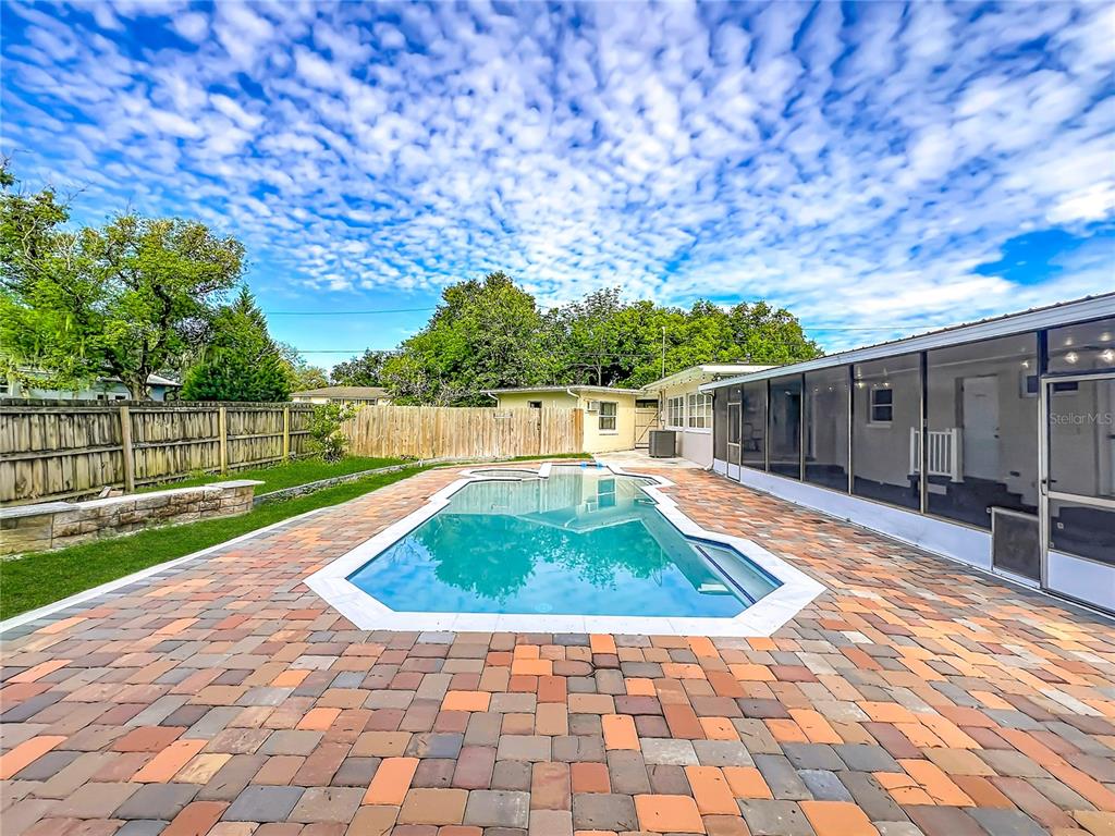 A backyard features a rectangular swimming pool surrounded by multicolored brick pavers and a wooden fence — 52 CLARK STREET, OVIEDO, FL