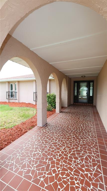 A covered entryway features a mosaic-tiled floor, arched columns, and a glass-paneled front door — 9737 SAN VINCENTE WAY, PORT RICHEY, FL
